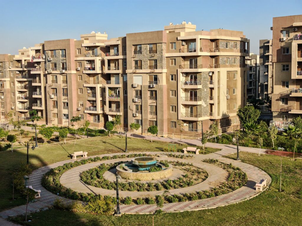 Aerial view of modern apartment buildings surrounding a landscaped garden on a sunny day.